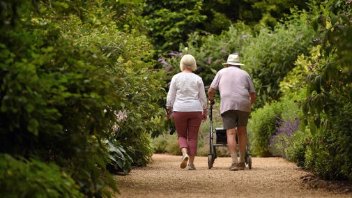 Two visitors, one using a walking frame, make their way down a track through the garden at Ascott, Buckinghamshire